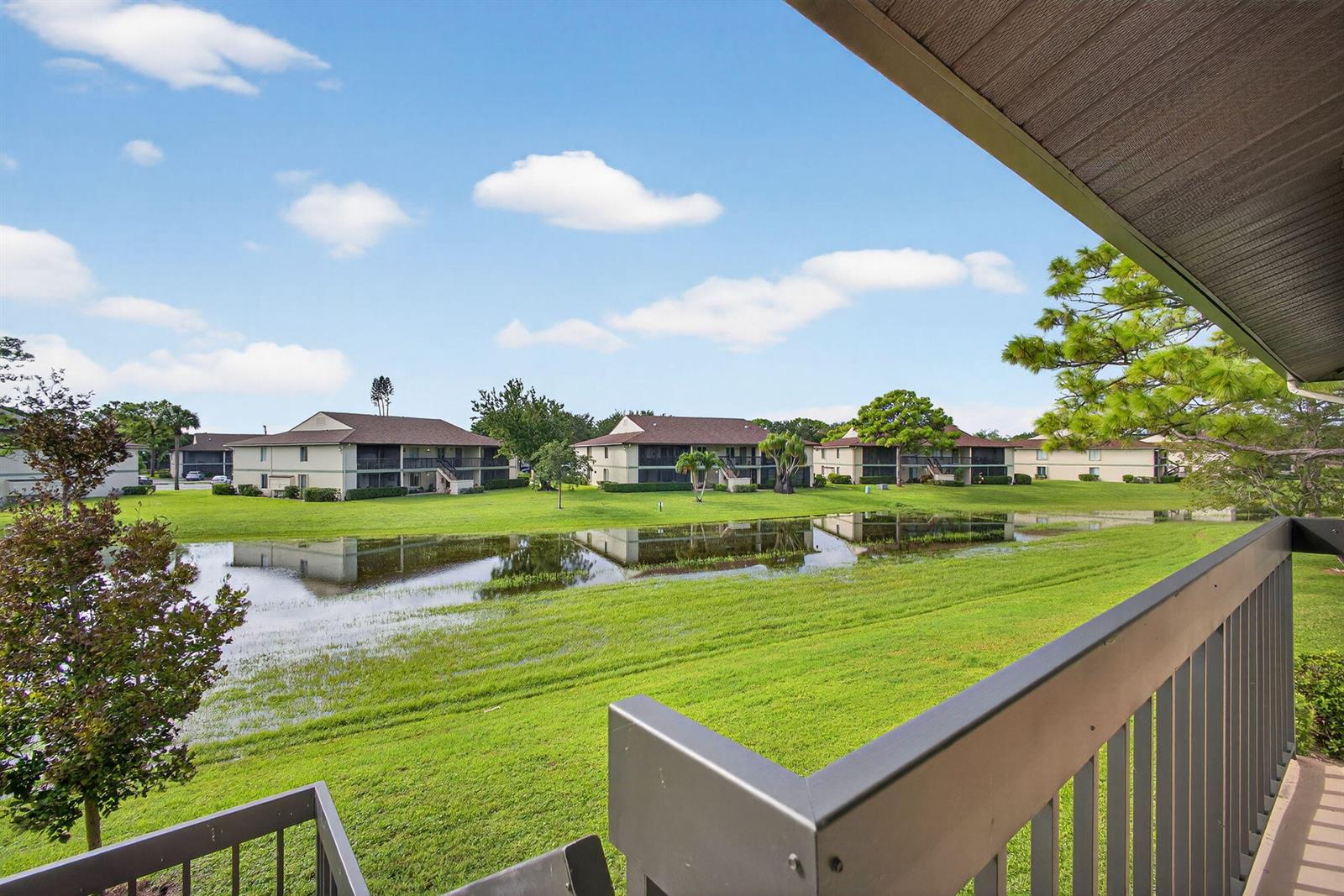 A view from a balcony overlooking a grassy lawn and a pond between apartment buildings — 6485 Chasewood Drive # G, Jupiter FL 33458, JUPITER, FL