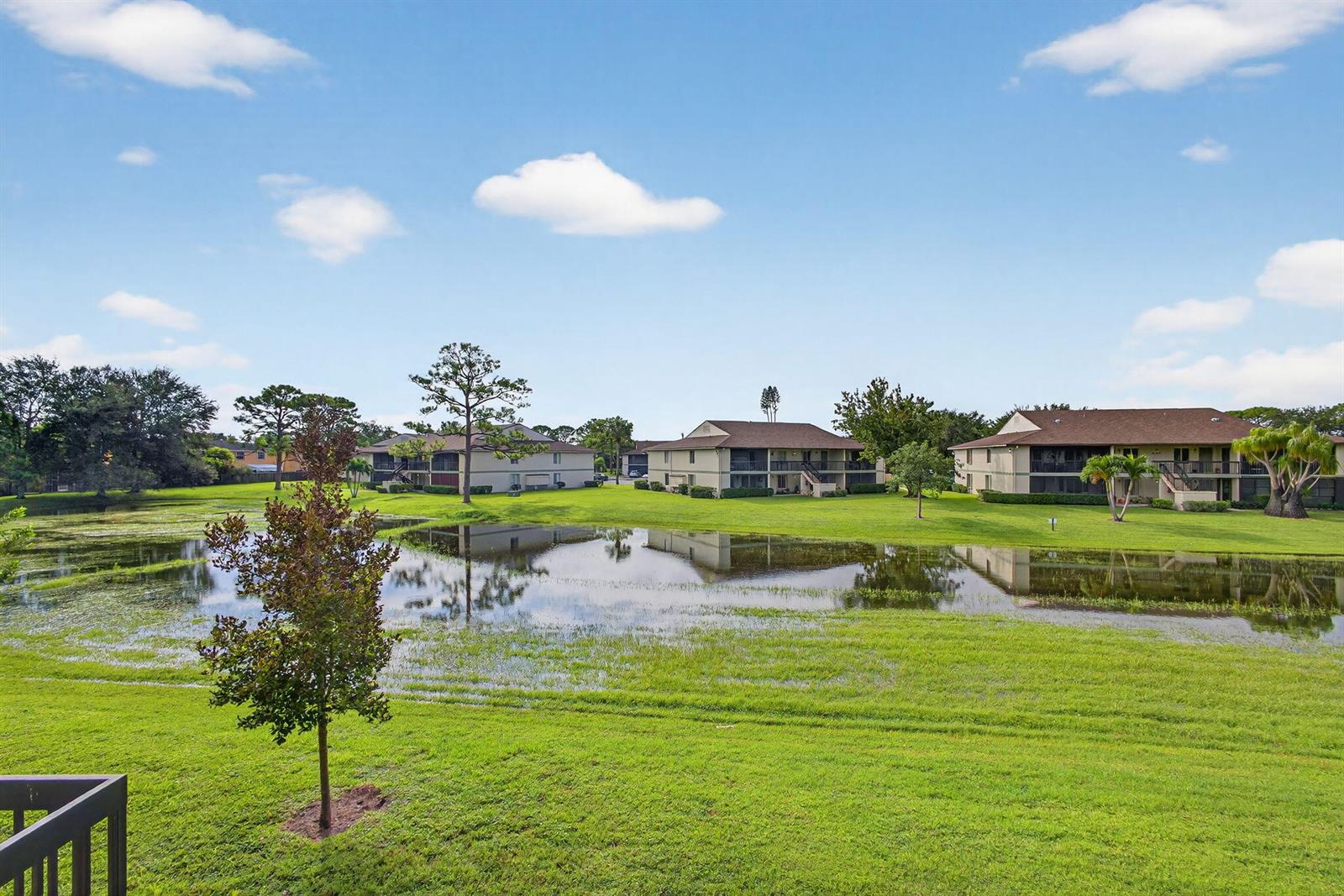 A view of a grassy lawn with a pond and several apartment buildings under sky — 6485 Chasewood Drive # G, Jupiter FL 33458, JUPITER, FL