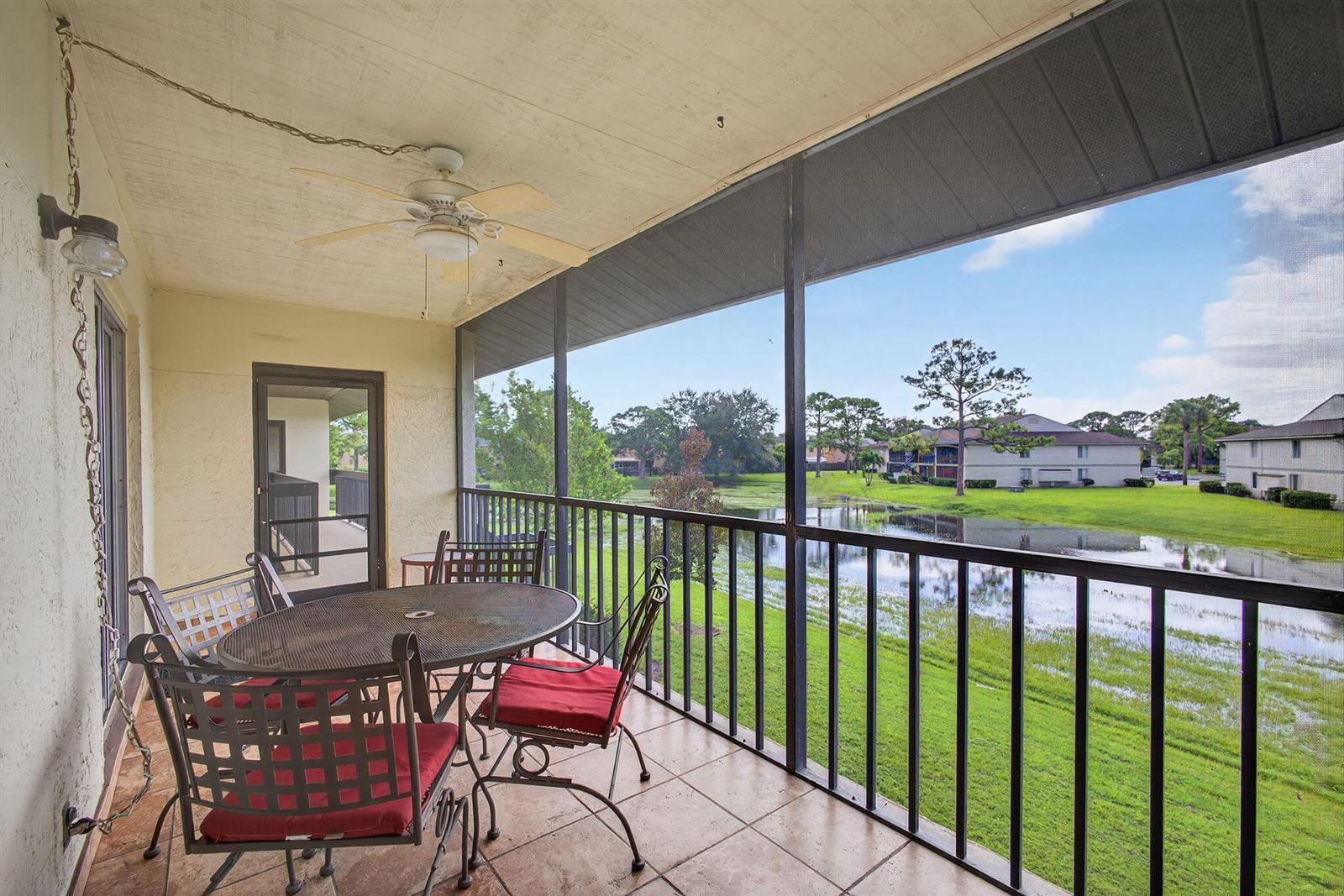 A screened-in balcony features a dining set, ceiling fan, and a view of a pond — 6485 Chasewood Drive # G, Jupiter FL 33458, JUPITER, FL