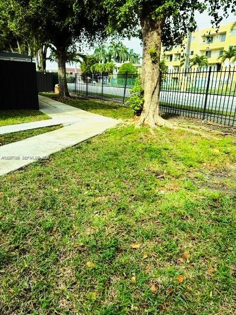 A grassy yard with a sidewalk leads toward a black fence and a yellow building — 680 NW 82nd. Pl. # 261, Miami FL 33126, MIAMI, FL