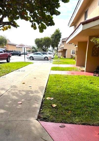 A sidewalk runs alongside a residential building with a lawn and parked cars nearby — 680 NW 82nd. Pl. # 261, Miami FL 33126, MIAMI, FL