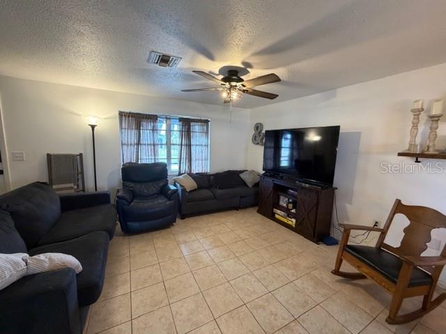 A living room features tile flooring, a ceiling fan, a television console, and various seating — 551 GROVE AVENUE NW, PORT CHARLOTTE, FL
