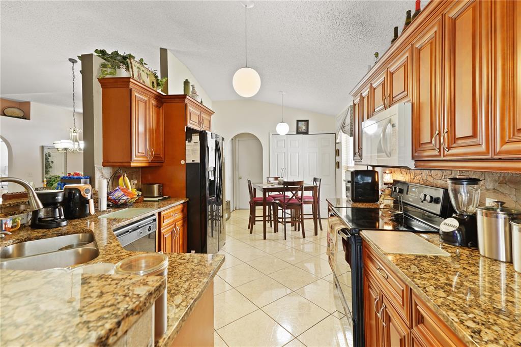 A kitchen with wood cabinets, granite countertops, and tile flooring opens to a dining area — 11545 BENTRY STREET, ORLANDO, FL