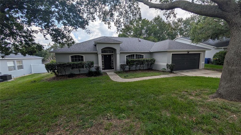 A single-story house with a gray exterior, a dark garage door, and a front walkway — 1306 WINDY BLUFF DRIVE, MINNEOLA, FL