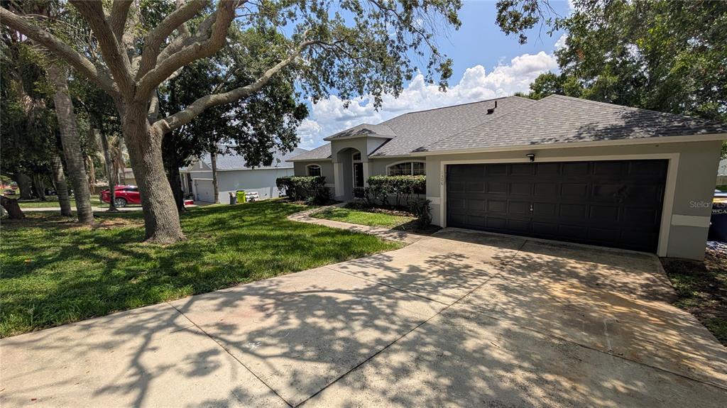 A single-story house with a dark garage door, a concrete driveway, and large shade trees — 1306 WINDY BLUFF DRIVE, MINNEOLA, FL