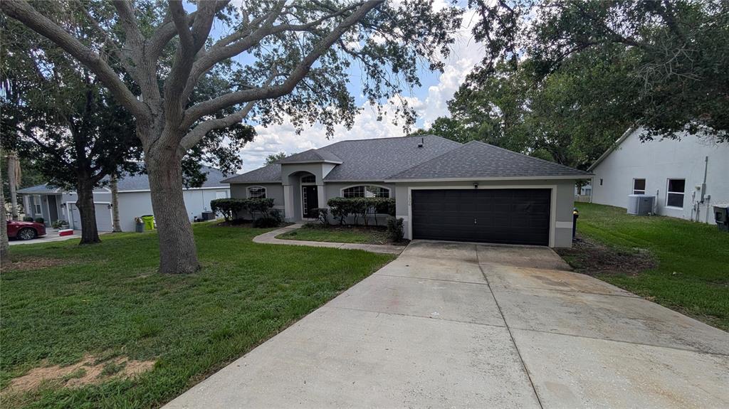 A single-story house with a gray roof, tan stucco exterior, and a two-car garage — 1306 WINDY BLUFF DRIVE, MINNEOLA, FL