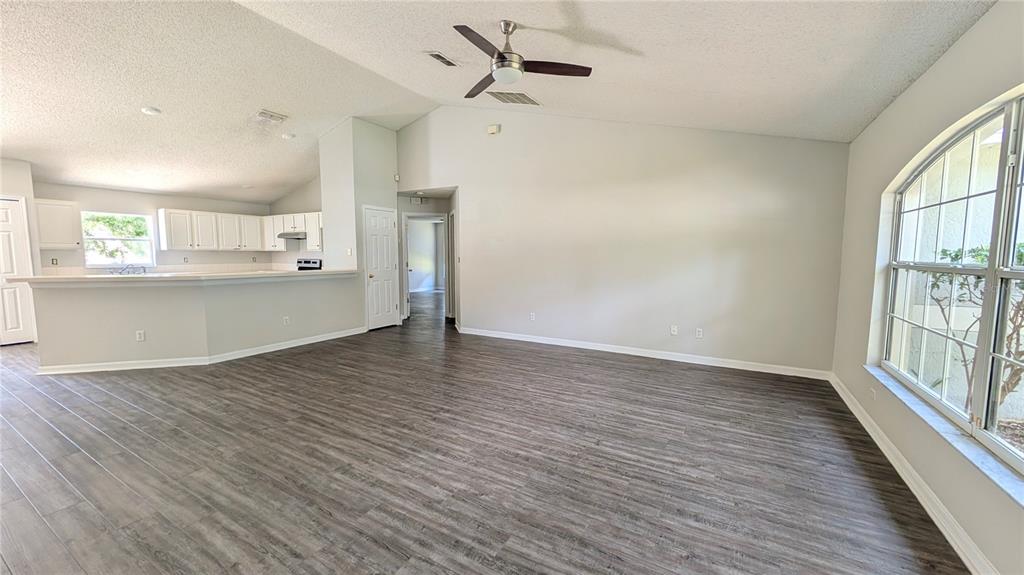 An open-concept living area features vaulted ceilings, wood-look flooring, and an adjacent kitchen with white cabinets — 1306 WINDY BLUFF DRIVE, MINNEOLA, FL