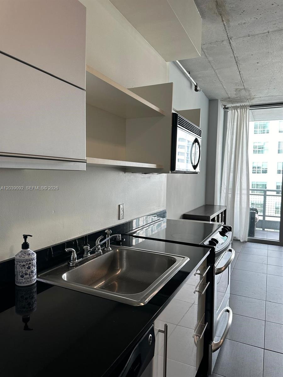 A modern kitchen features black countertops, stainless steel appliances, and an adjacent balcony with curtains — 690 SW 1st Ct # 2328, Miami FL 33130, MIAMI, FL