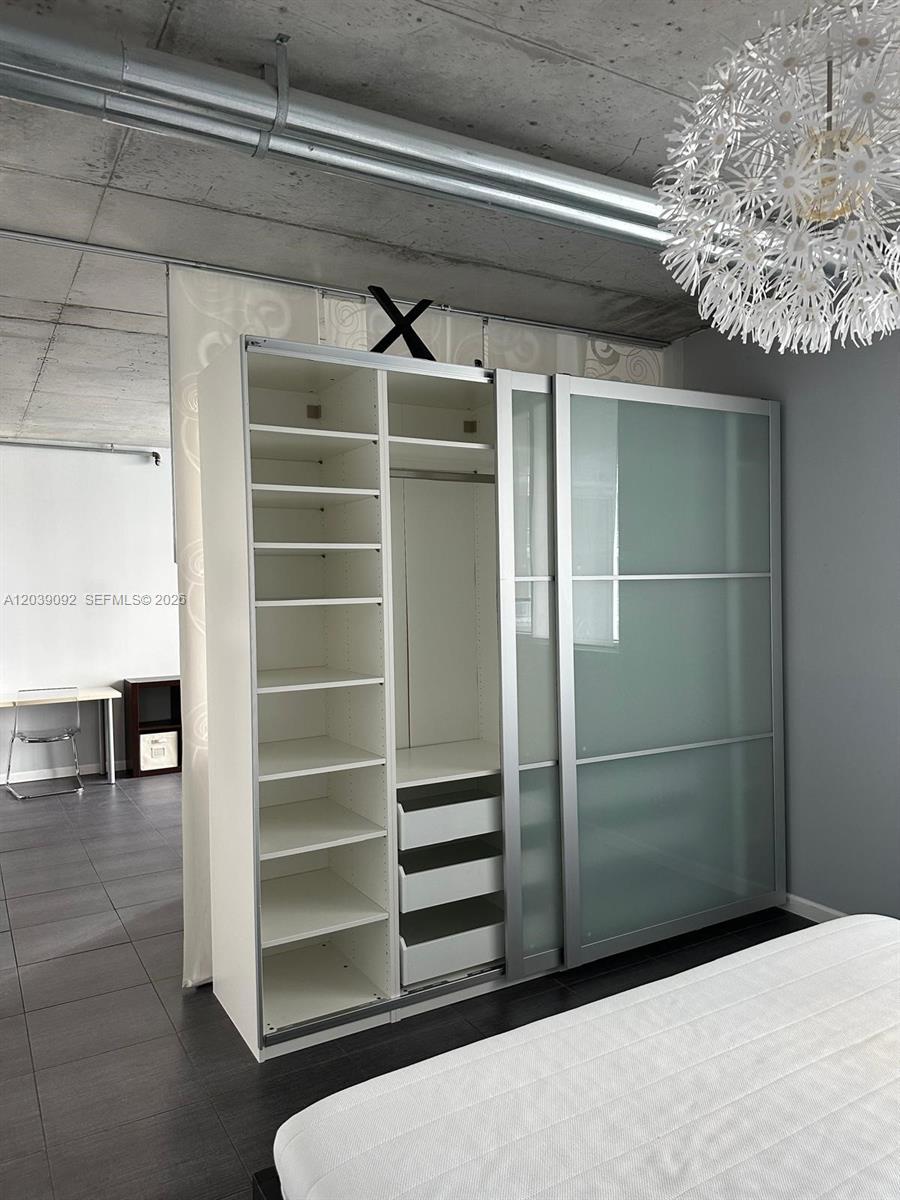 A bedroom features a large white sliding-door wardrobe with open shelving and a modern chandelier — 690 SW 1st Ct # 2328, Miami FL 33130, MIAMI, FL