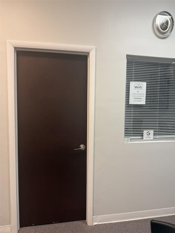 A dark brown door stands next to a window with blinds and a wall clock — 12250 MENTA STREET UNIT 105, ORLANDO, FL
