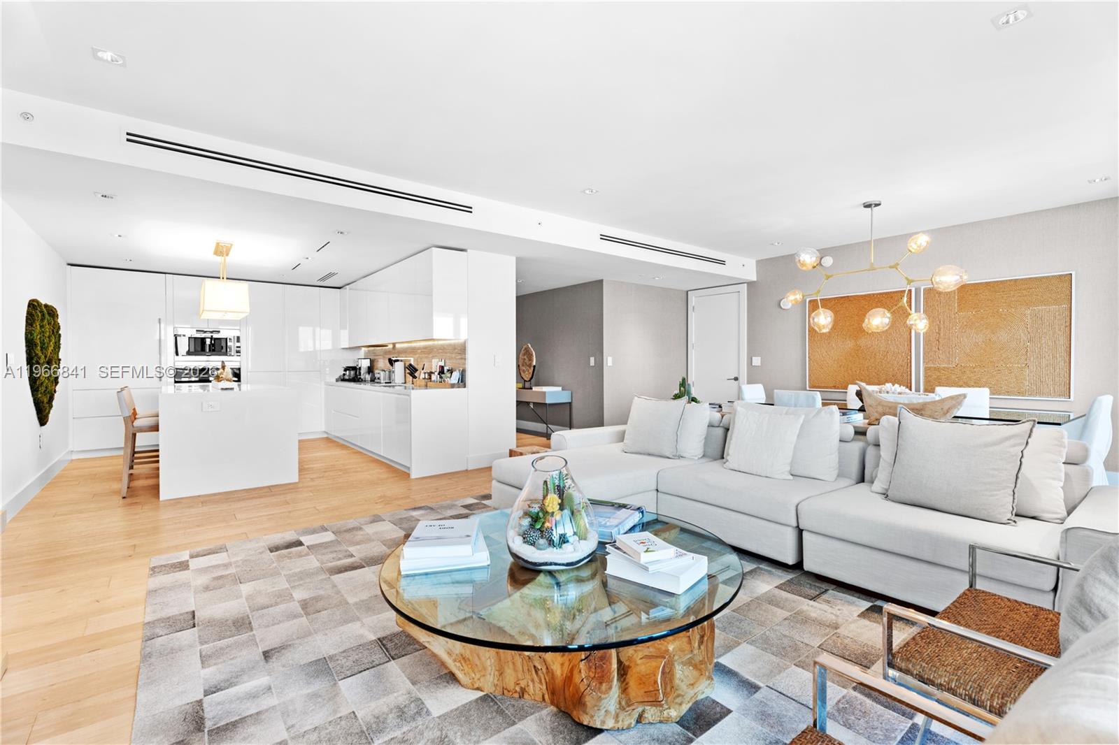 A modern open-concept living room features a white kitchen, sectional sofa, and glass coffee table — 102 24th St # 1705, Miami Beach FL 33139, MIAMI BEACH, FL