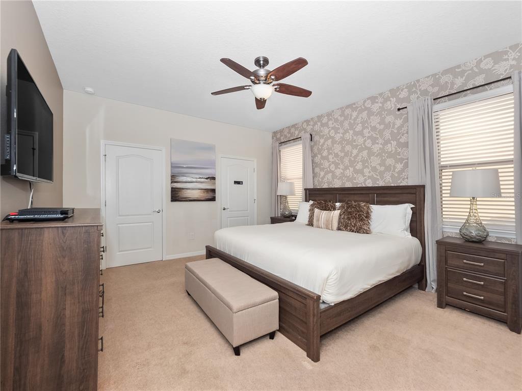 A bedroom features a king-sized bed, patterned wallpaper, a ceiling fan, and a wooden dresser — 8825 RHODES STREET, KISSIMMEE, FL