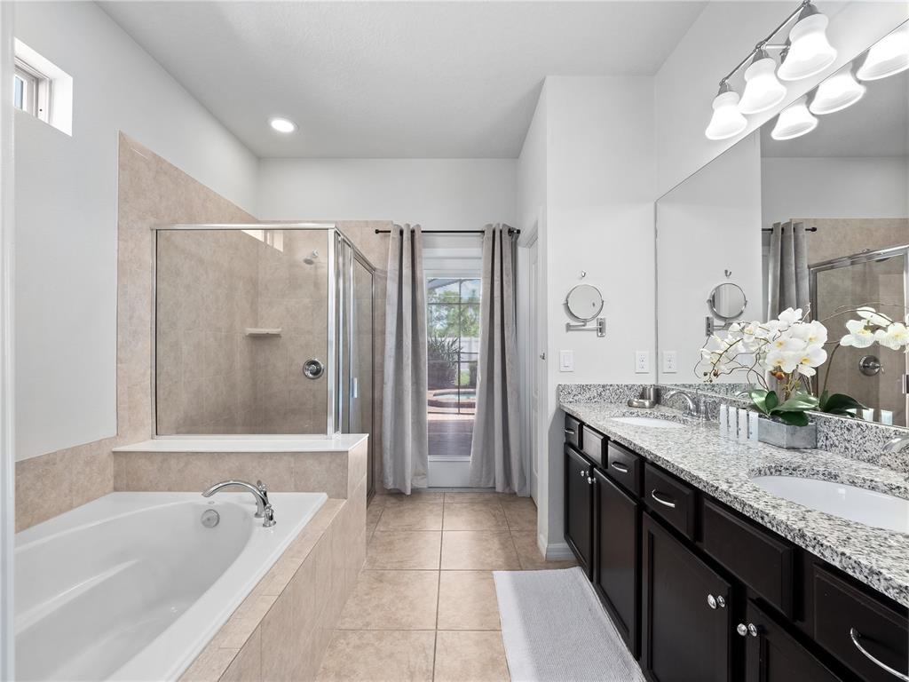 A bathroom features a soaking tub, a glass-enclosed shower, and a double vanity with granite — 8825 RHODES STREET, KISSIMMEE, FL
