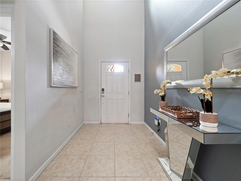 A bright entryway features a white front door, tiled floors, a mirrored console table, and artwork — 8825 RHODES STREET, KISSIMMEE, FL