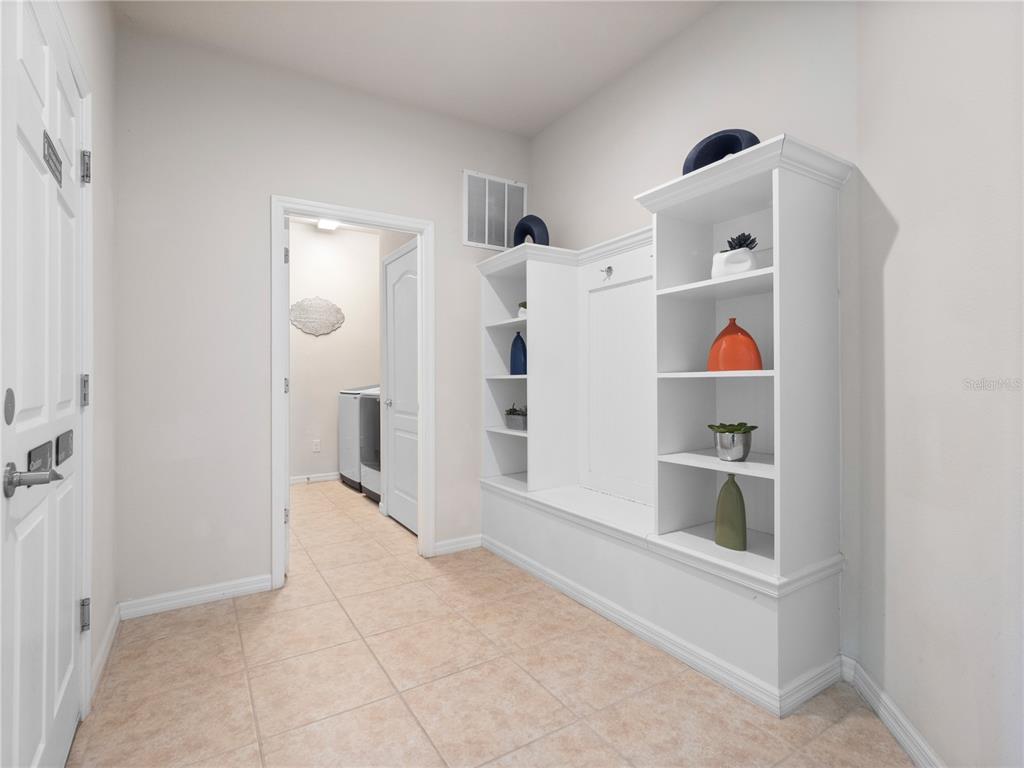A mudroom features a white built-in storage bench with shelving and tile flooring — 8825 RHODES STREET, KISSIMMEE, FL