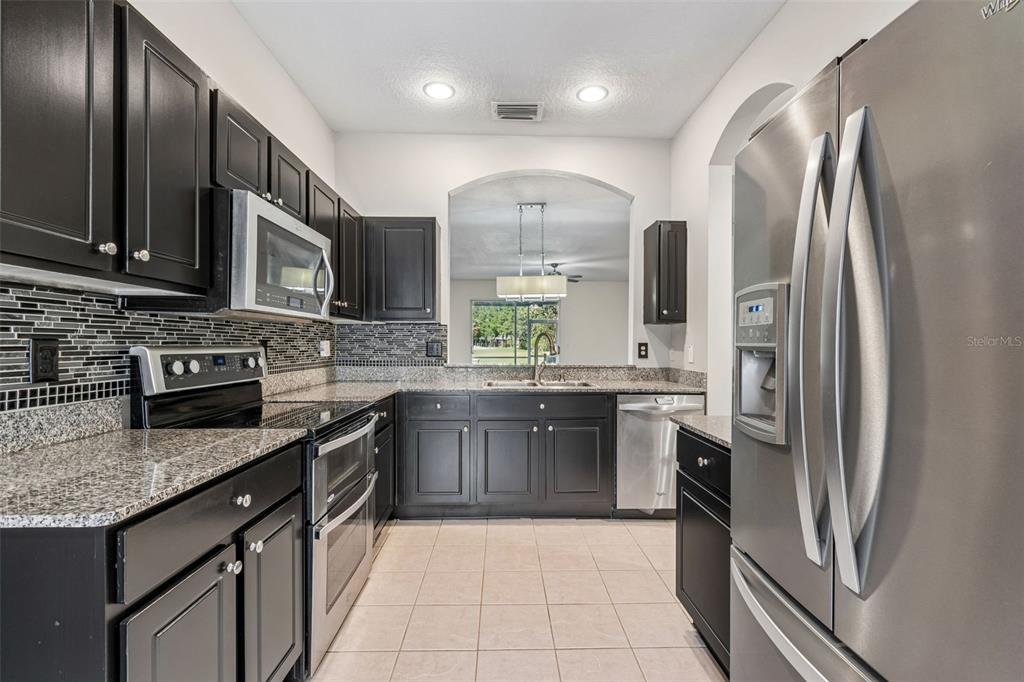 A kitchen features dark cabinets, granite countertops, stainless steel appliances, and a tiled floor — 18107 NASSAU POINT DR, TAMPA, FL