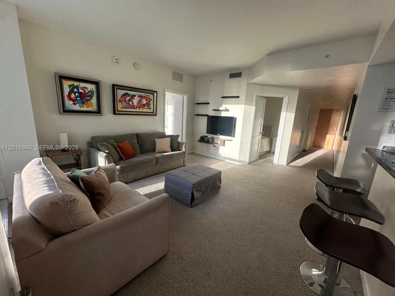 A living room features a sofa, loveseat, ottoman, wall-mounted television, and a breakfast bar — 253 NE 2nd St # 1402, Miami FL 33132, MIAMI, FL