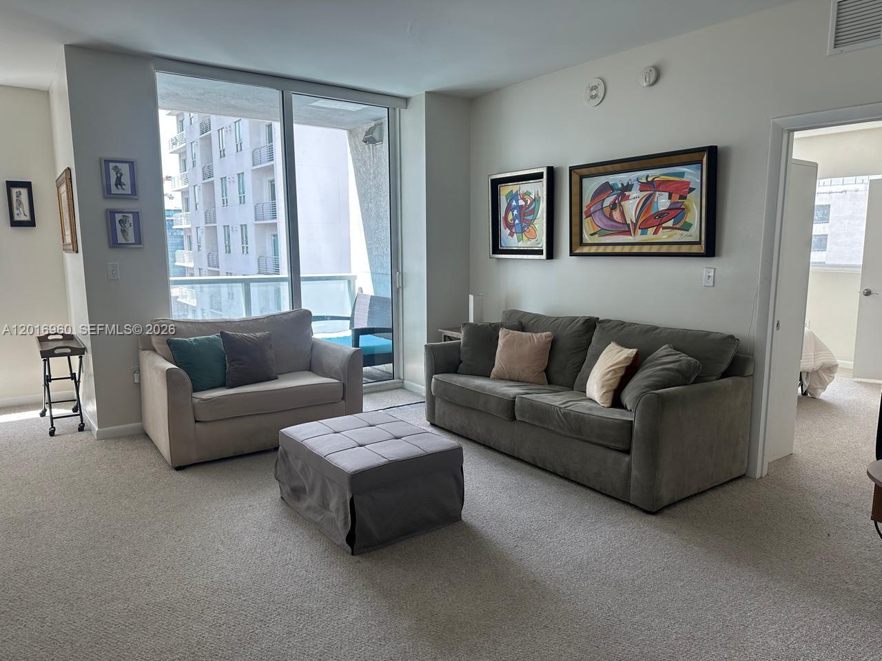 A living room features a sofa, loveseat, ottoman, and large windows overlooking a balcony — 253 NE 2nd St # 1402, Miami FL 33132, MIAMI, FL