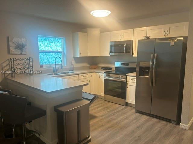 A kitchen features white cabinetry, stainless steel appliances, a breakfast bar, and light wood flooring — 1497 Las Villas Blvd, Sebring FL 33870, SEBRING, FL