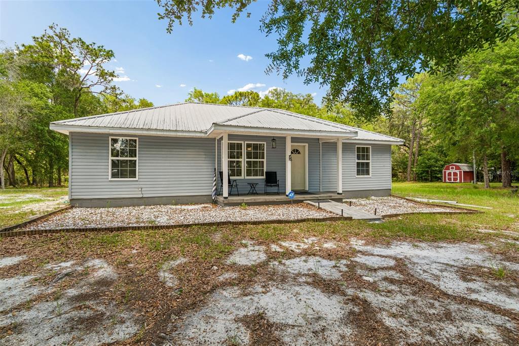 A single-story light blue house with a metal roof sits on a sandy lot — 8855 SW 146TH PLACE, DUNNELLON, FL