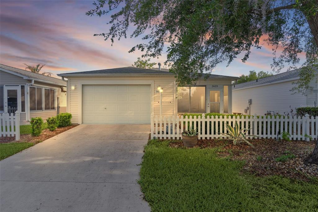 A single-story house with a garage, white picket fence, and driveway at sunset — 2623 ASCOT LOOP, THE VILLAGES, FL