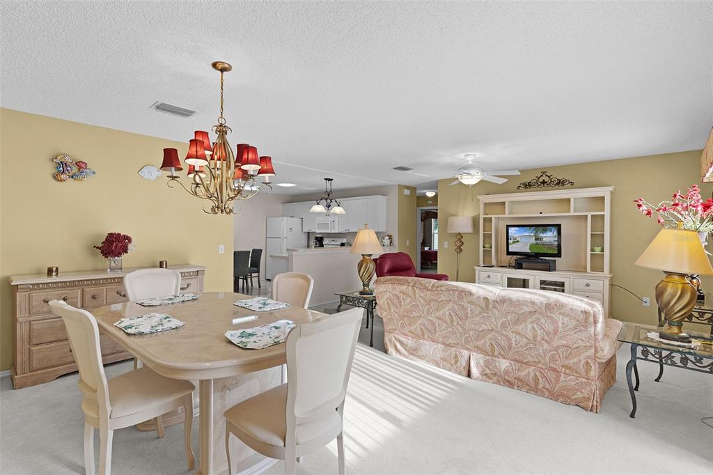A dining area with a chandelier and table flows into a living room with seating — 2623 ASCOT LOOP, THE VILLAGES, FL