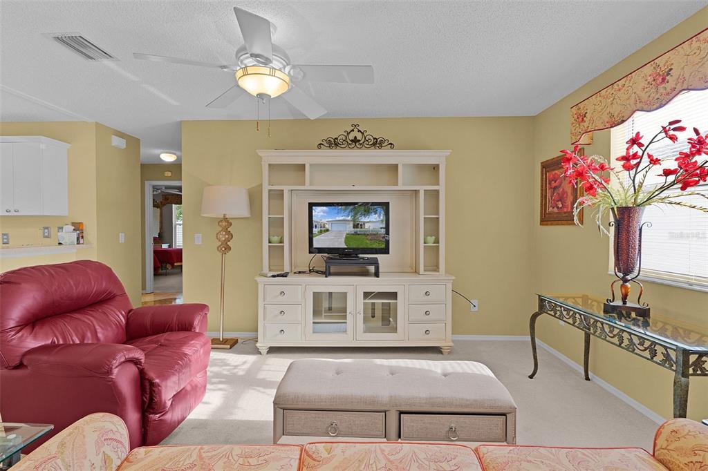 A living room features a red leather armchair, a white entertainment center, and a beige ottoman — 2623 ASCOT LOOP, THE VILLAGES, FL