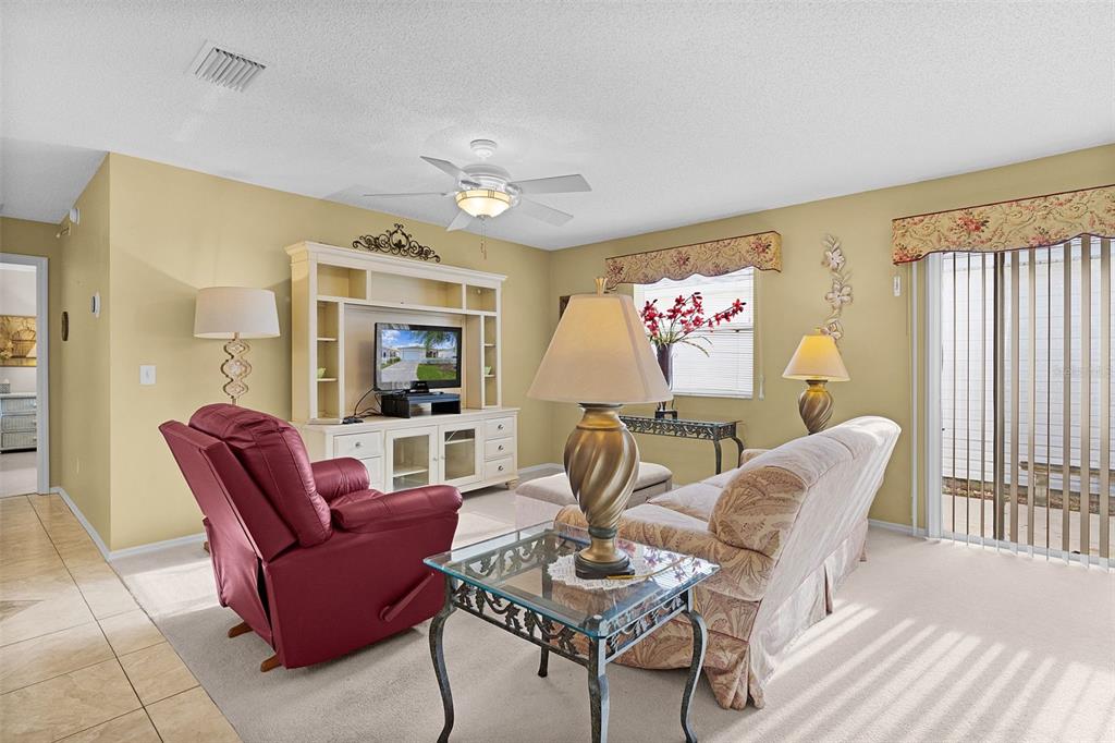 A living room features a red recliner, a patterned sofa, and a white entertainment center — 2623 ASCOT LOOP, THE VILLAGES, FL