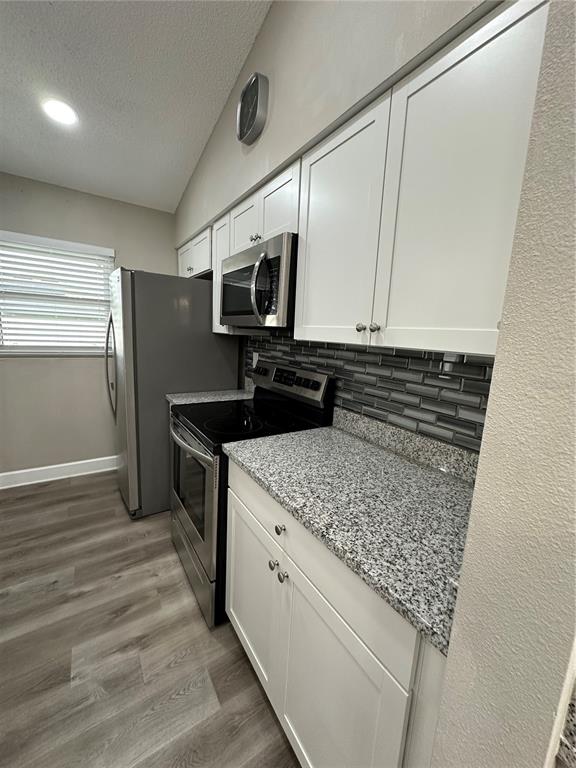 A kitchen features white cabinets, granite countertops, a gray tiled backsplash, and stainless steel appliances — 1229 ALLENDALE DRIVE, OVIEDO, FL