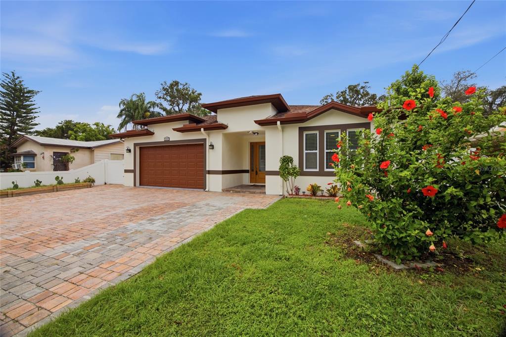 A single-story house with a brown garage door, paved driveway, and a blooming hibiscus bush — 1707 E EMMA STREET, TAMPA, FL