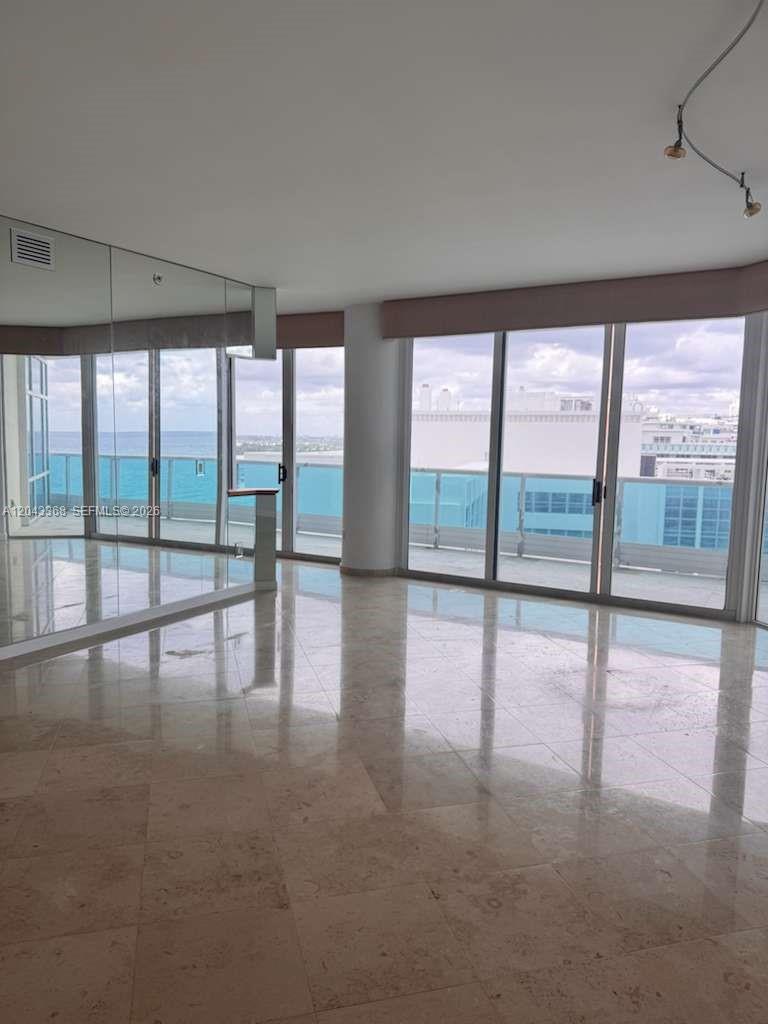 An empty room with marble floors, mirrored walls, and floor-to-ceiling windows overlooking the ocean — 5025 Collins Ave # 1602, Miami Beach FL 33140, MIAMI BEACH, FL