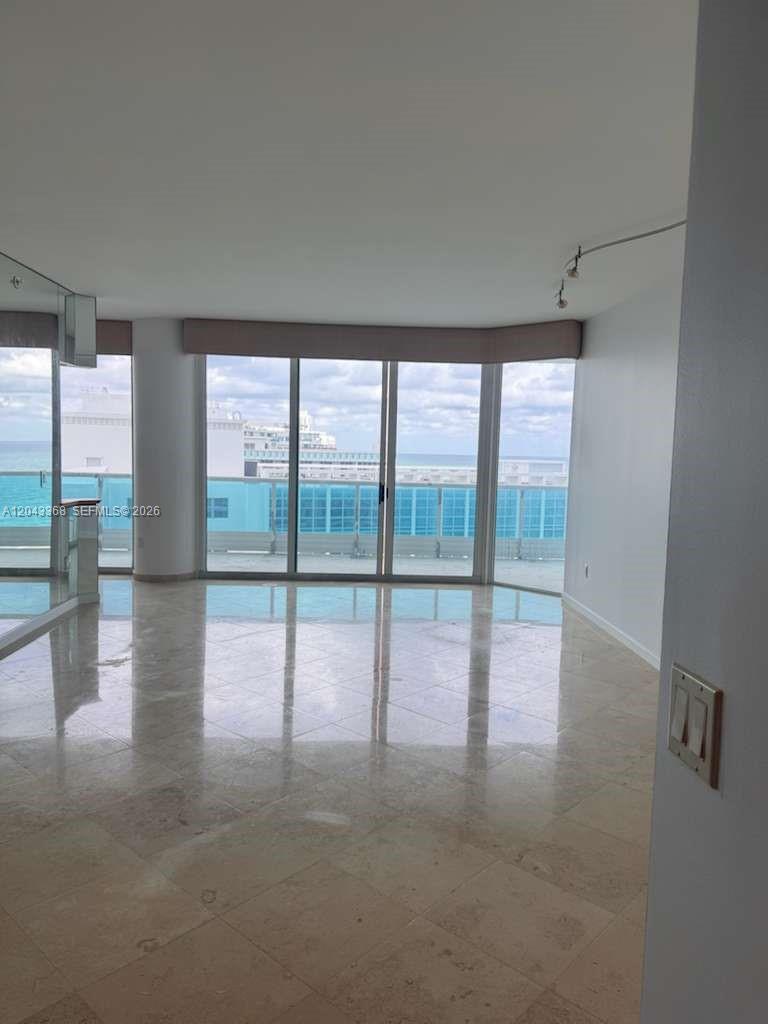 An empty room with light-colored tile flooring features floor-to-ceiling windows overlooking the ocean — 5025 Collins Ave # 1602, Miami Beach FL 33140, MIAMI BEACH, FL