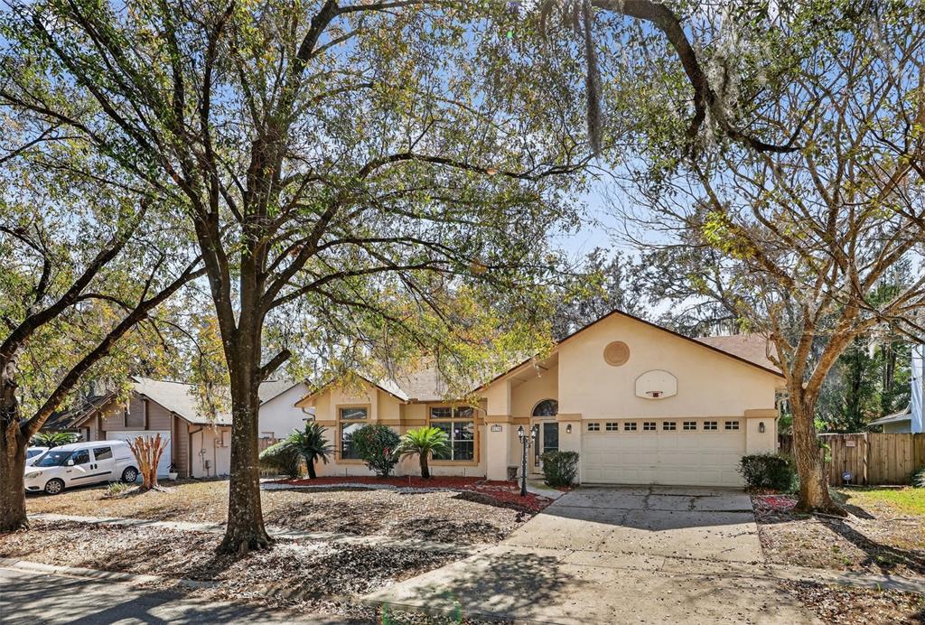 A single-story house with a beige stucco exterior, a two-car garage, and mature trees — 3236 PAISLEY CIRCLE, ORLANDO, FL