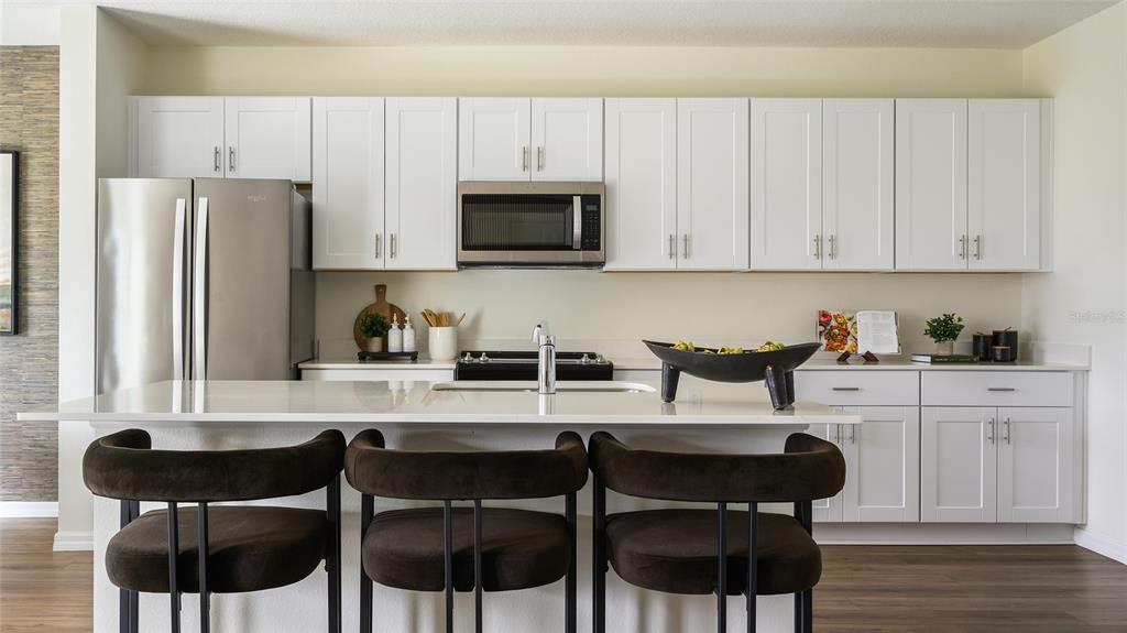 A modern kitchen features white cabinetry, stainless steel appliances, a quartz island, and three stools — 33561 NOBLE CREEK PLACE, DADE CITY, FL