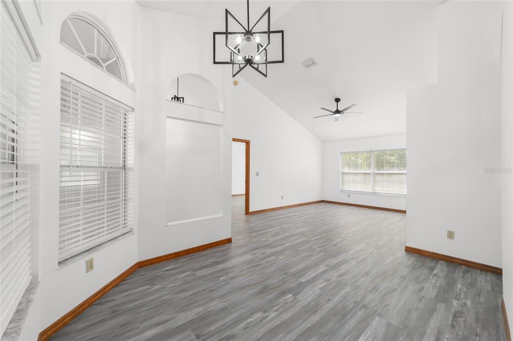 A bright, empty living room features vaulted ceilings, gray wood-look flooring, and a geometric chandelier — 13984 SW 80TH STREET, DUNNELLON, FL