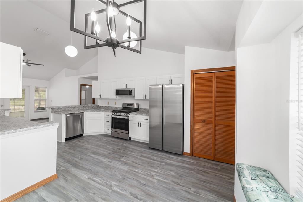 A kitchen with white cabinets, stainless steel appliances, a large chandelier, and gray wood flooring — 13984 SW 80TH STREET, DUNNELLON, FL