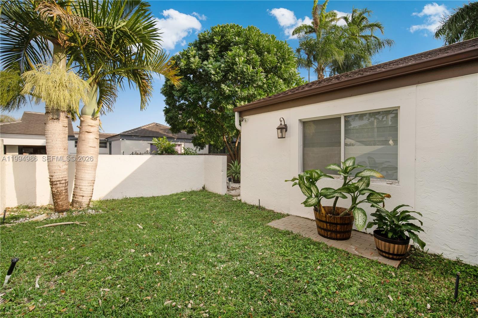 A grassy backyard features a white stucco wall, two palm trees, and potted plants — 15250 SW 154th Ter # A, Miami FL 33187, MIAMI, FL