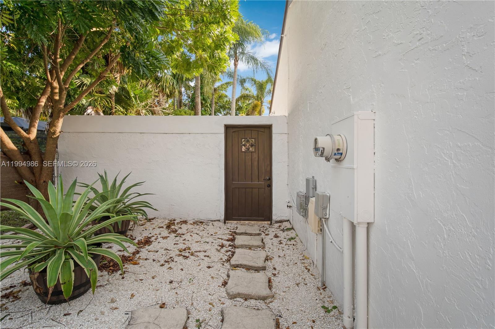 A wooden door set in a white stucco wall leads to a gravel courtyard — 15250 SW 154th Ter # A, Miami FL 33187, MIAMI, FL