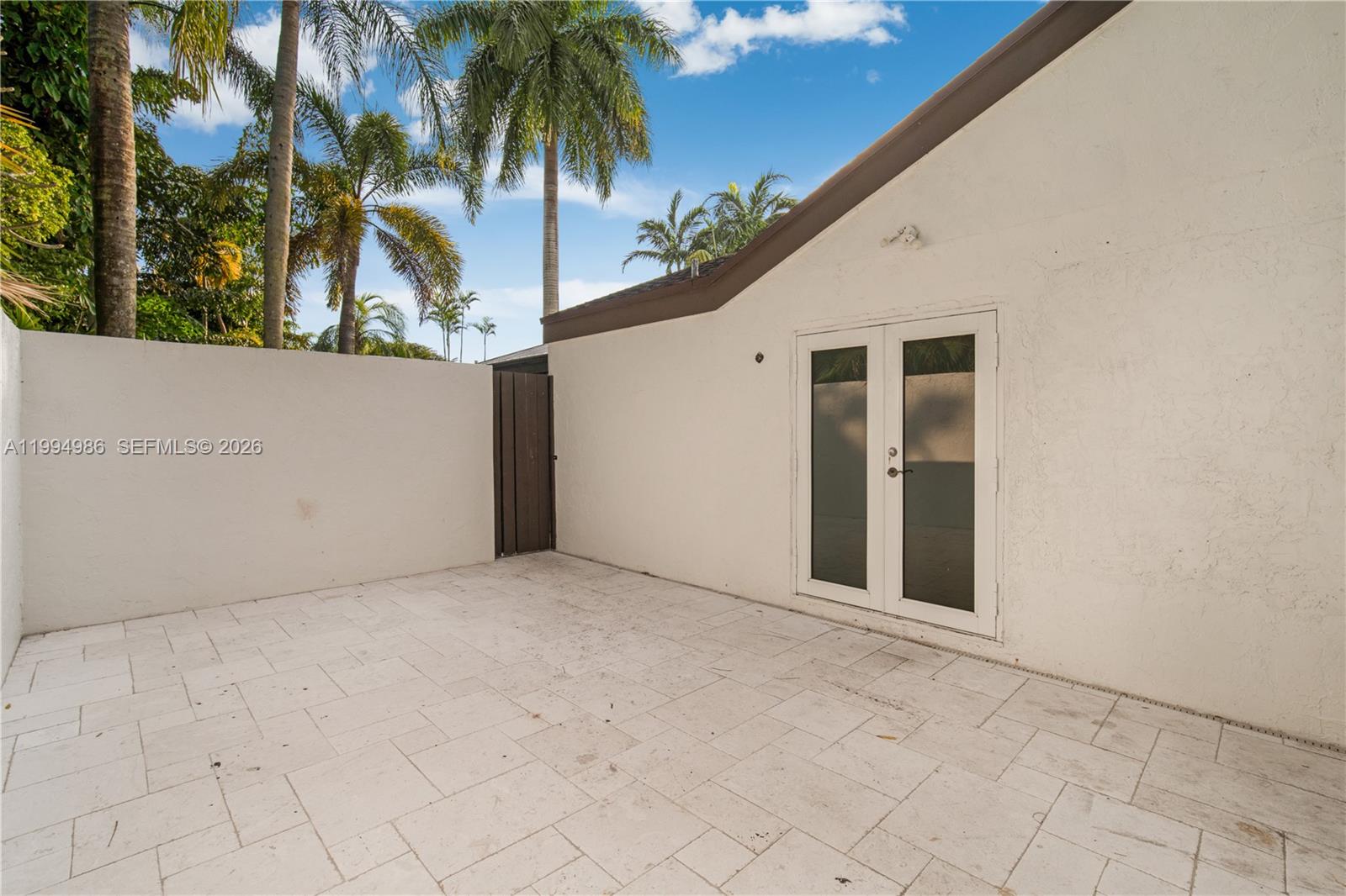 A paved patio area features a white stucco wall, a wooden gate, and French doors — 15250 SW 154th Ter # A, Miami FL 33187, MIAMI, FL