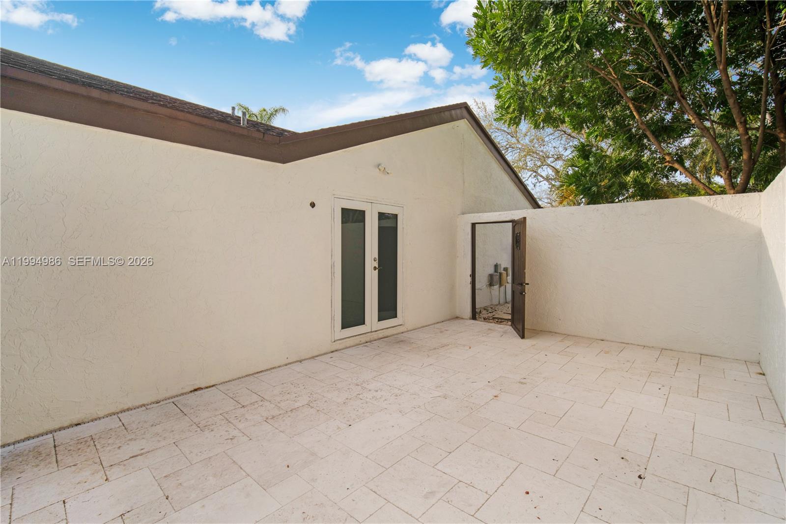 A paved patio features a white stucco wall, double glass doors, and an open gate — 15250 SW 154th Ter # A, Miami FL 33187, MIAMI, FL