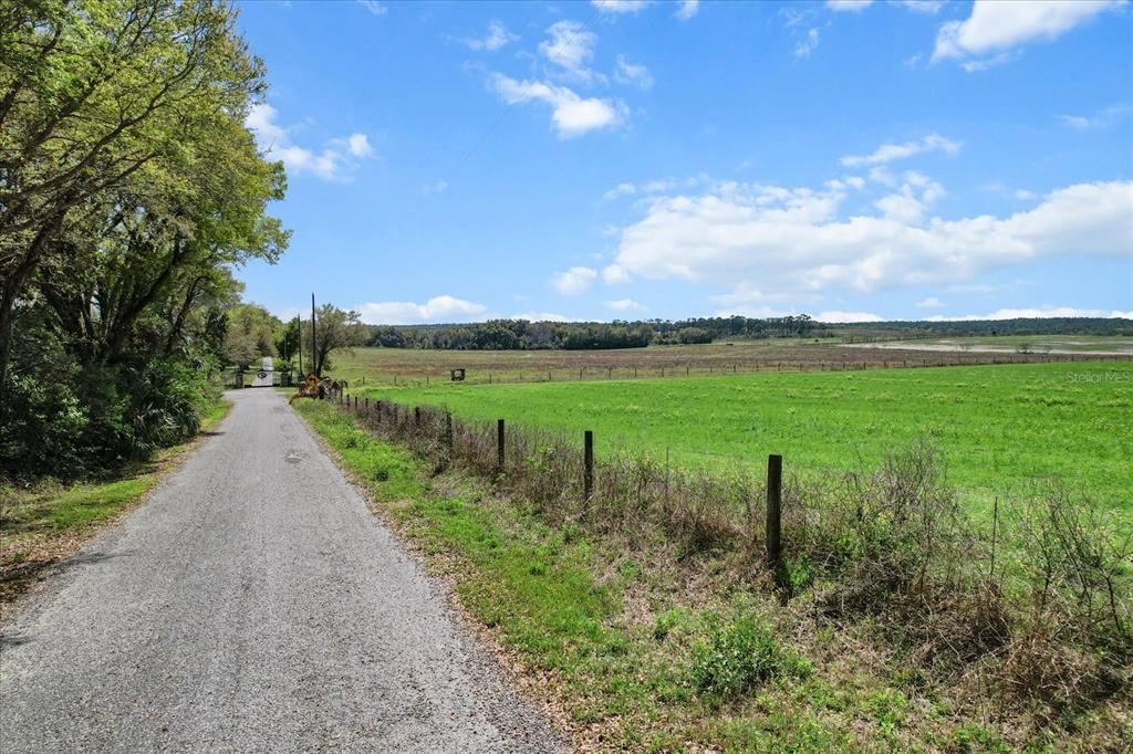 A gravel road runs alongside a fenced green pasture under a blue sky with clouds — (190 AC-see addt'l PID's) NW 225TH AVENUE, DUNNELLON, FL