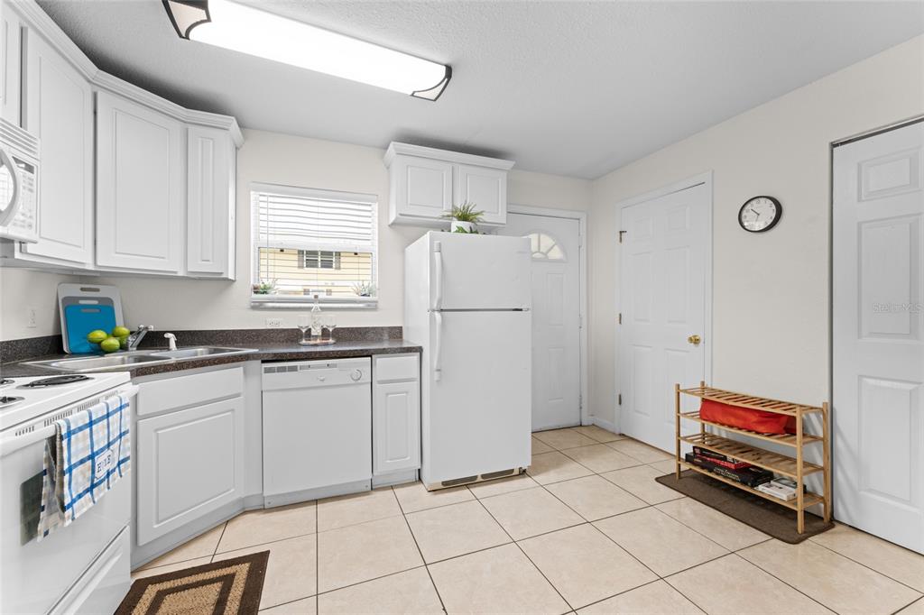 A kitchen features white cabinets, white appliances, tile flooring, and a small wooden shoe rack — 4420 CARTER ROAD UNIT 47, ST AUGUSTINE, FL