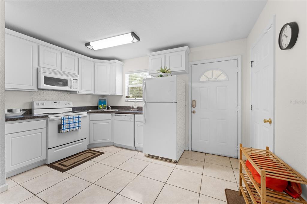 A kitchen features white cabinets, white appliances, tiled floors, and a door leading outside — 4420 CARTER ROAD UNIT 47, ST AUGUSTINE, FL