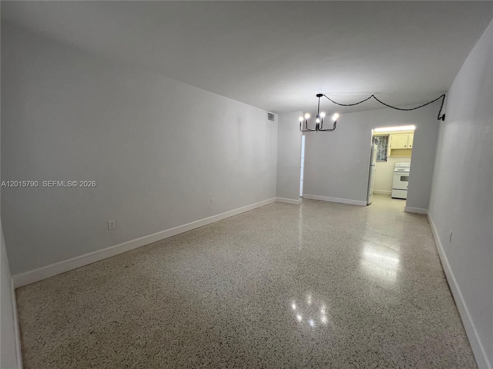 An empty room with white walls, a chandelier, and polished terrazzo flooring — 675 SW 7th Ave # 2, Miami FL 33130, MIAMI, FL