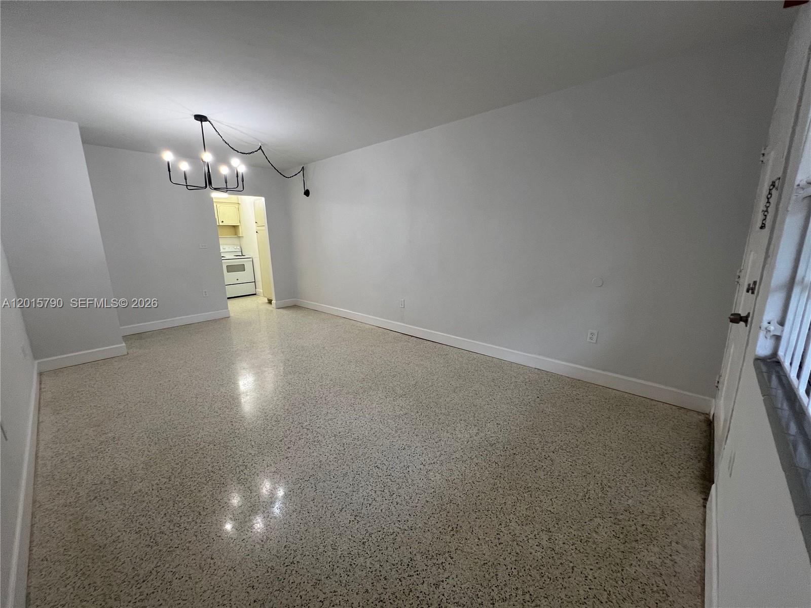An empty living room features white walls, a modern chandelier, and speckled terrazzo flooring — 675 SW 7th Ave # 2, Miami FL 33130, MIAMI, FL