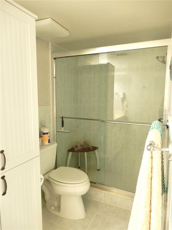 A bathroom features a white toilet, a glass-enclosed shower, and a tall white storage cabinet — 103 1ST STREET E UNIT 210, TIERRA VERDE, FL