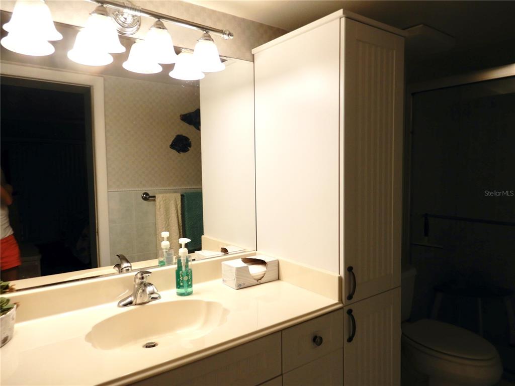 A bathroom vanity features a white countertop, sink, large mirror, and a tall storage cabinet — 103 1ST STREET E UNIT 210, TIERRA VERDE, FL