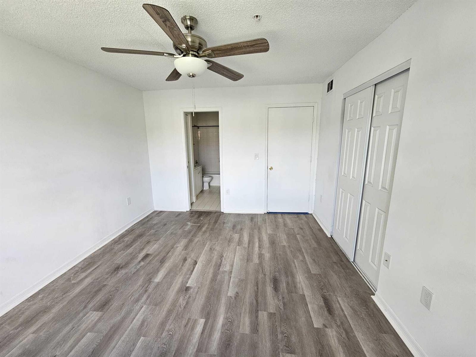 An empty bedroom features gray wood-look flooring, a ceiling fan, and two white doors — 12154 St.andrews Place # 206, Miramar FL 33025, MIRAMAR, FL