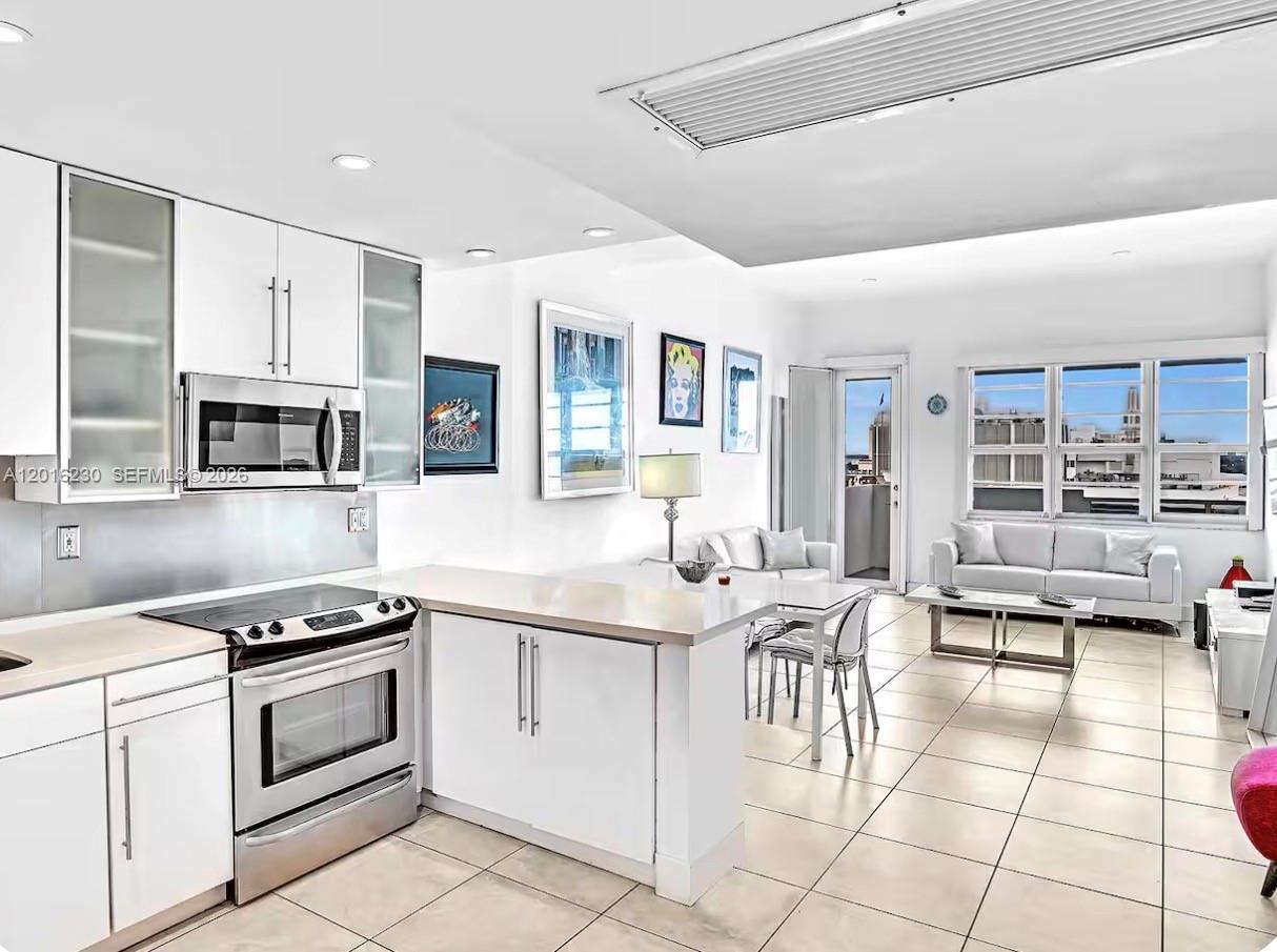 A bright, open-concept kitchen and living area features white cabinetry, tile flooring, and large windows — 100 Lincoln Rd # 1641, Miami Beach FL 33139, MIAMI BEACH, FL