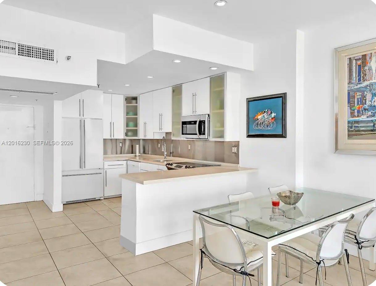 A modern kitchen with white cabinets and a glass-topped dining table in the foreground — 100 Lincoln Rd # 1641, Miami Beach FL 33139, MIAMI BEACH, FL